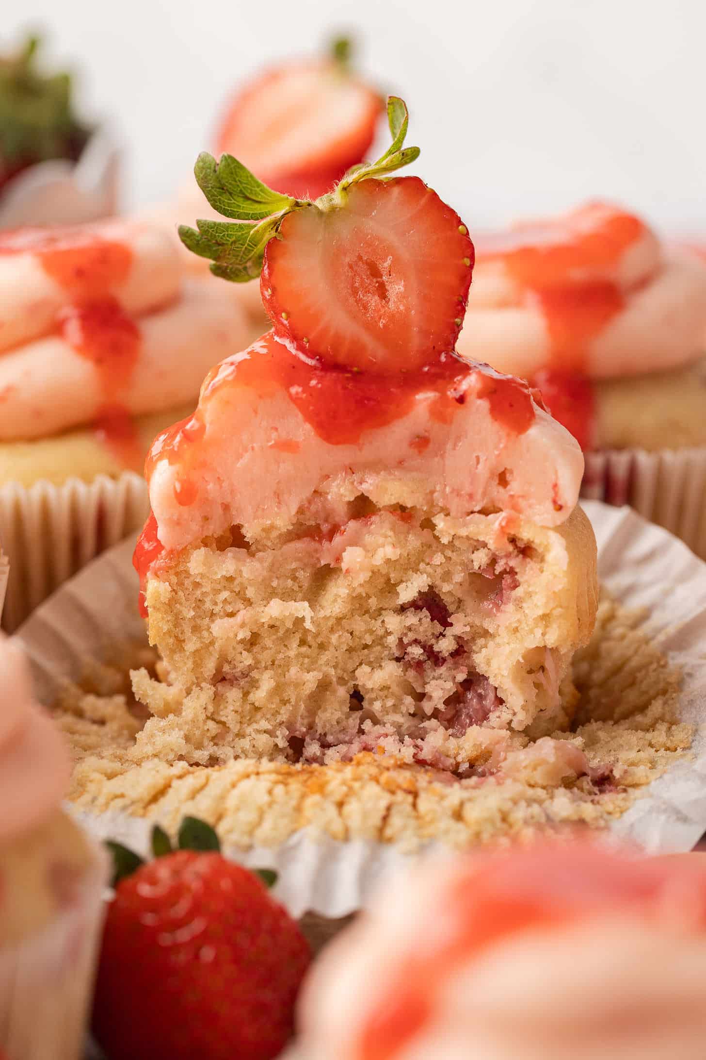 Inside view of a strawberry cupcake split open to reveal a soft, fluffy crumb filled with chunks of fresh strawberry, topped with pink buttercream and a fresh strawberry slice