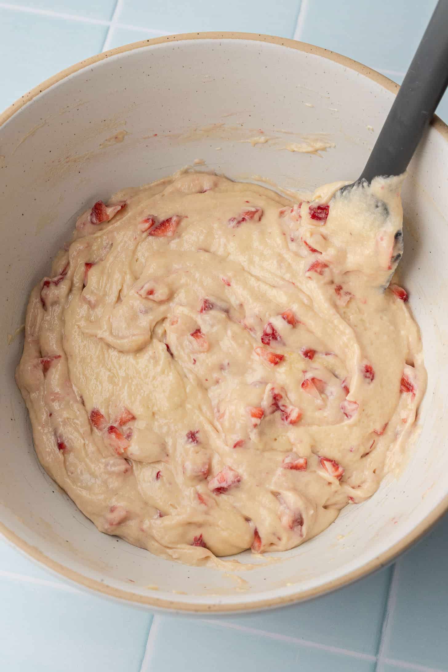 Vanilla cupcake batter studded with diced fresh strawberry pieces in a ceramic bowl, ready to be scooped into the cupcake tin