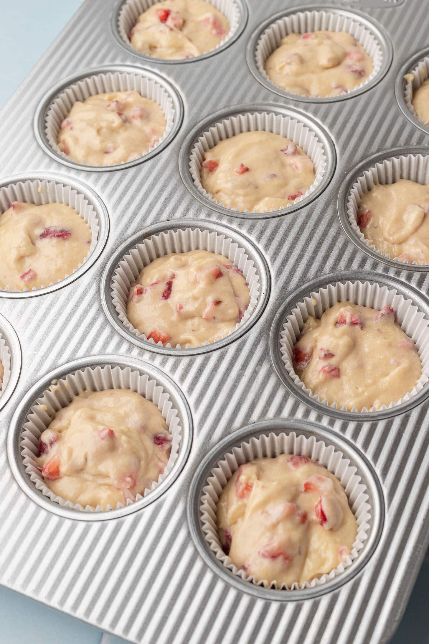 Strawberry cupcake batter divided into a silver cupcake tin lined with white parchment liners, ready to bake