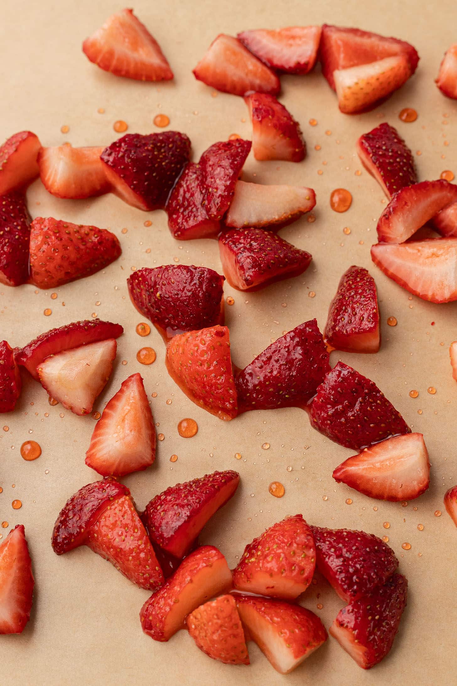 Sliced fresh strawberries tossed in sugar and lemon juice spread out on parchment paper, ready to roast