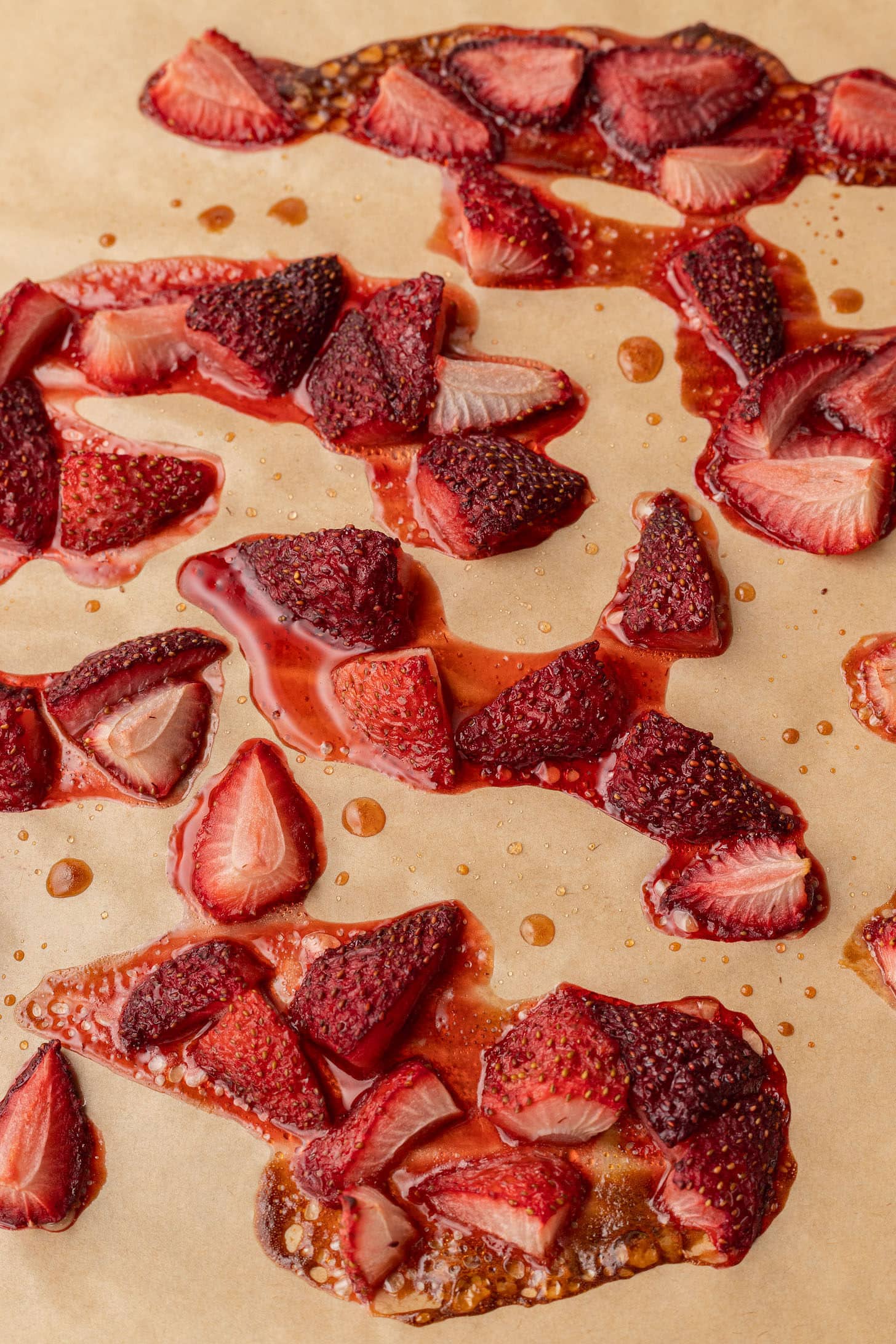 Roasted strawberries on parchment paper after baking, deeply caramelized and jammy with pools of concentrated strawberry syrup