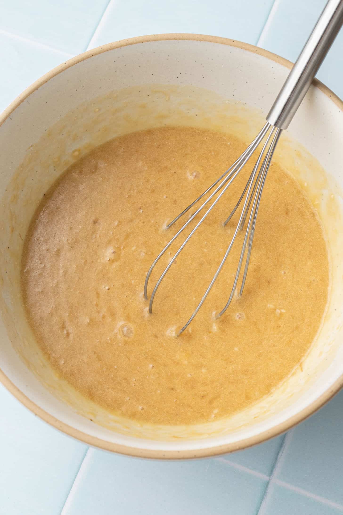 Banana muffin wet ingredients whisked together in a cream-colored ceramic bowl until smooth and golden