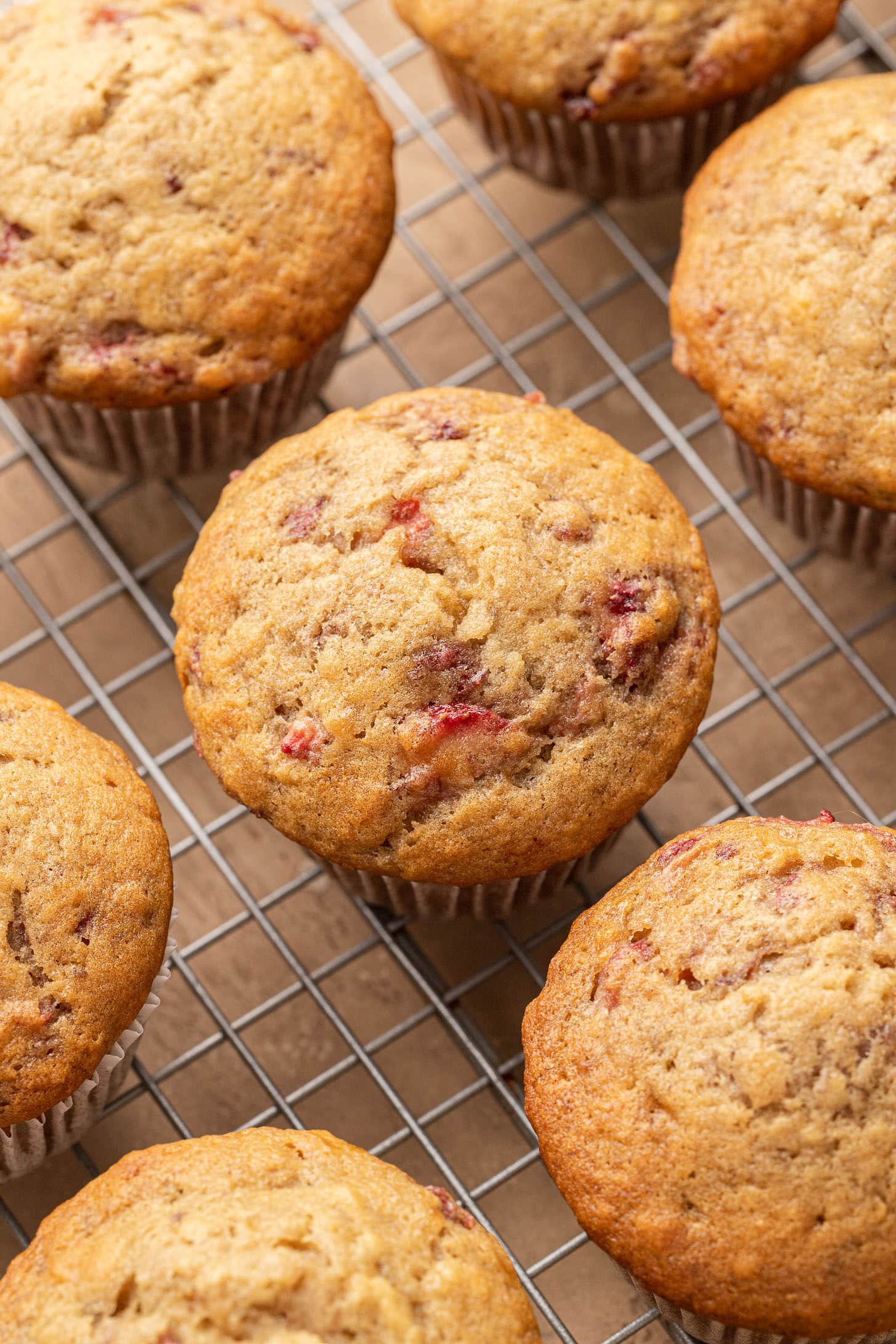 Freshly baked strawberry banana muffins with golden domed tops cooling on a wire rack, studded with bits of roasted strawberry