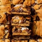 Three s'mores cookie bars stacked on top of each other, showing the distinct layers of graham cracker, gooey marshmallow, melted chocolate, and golden cookie dough