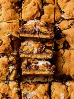 Three s'mores cookie bars stacked on top of each other, showing the distinct layers of graham cracker, gooey marshmallow, melted chocolate, and golden cookie dough