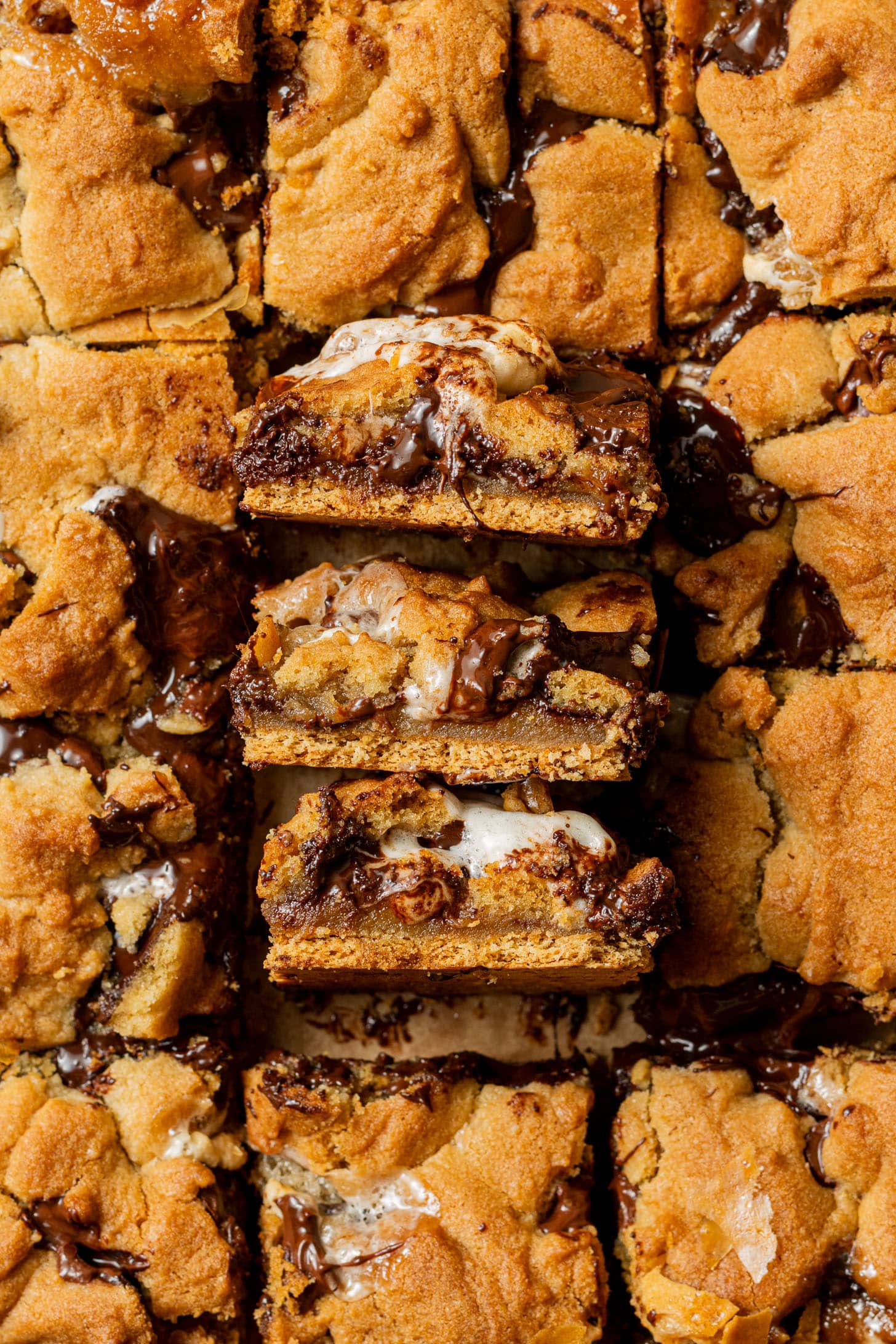 Three s'mores cookie bars stacked on top of each other, showing the distinct layers of graham cracker, gooey marshmallow, melted chocolate, and golden cookie dough