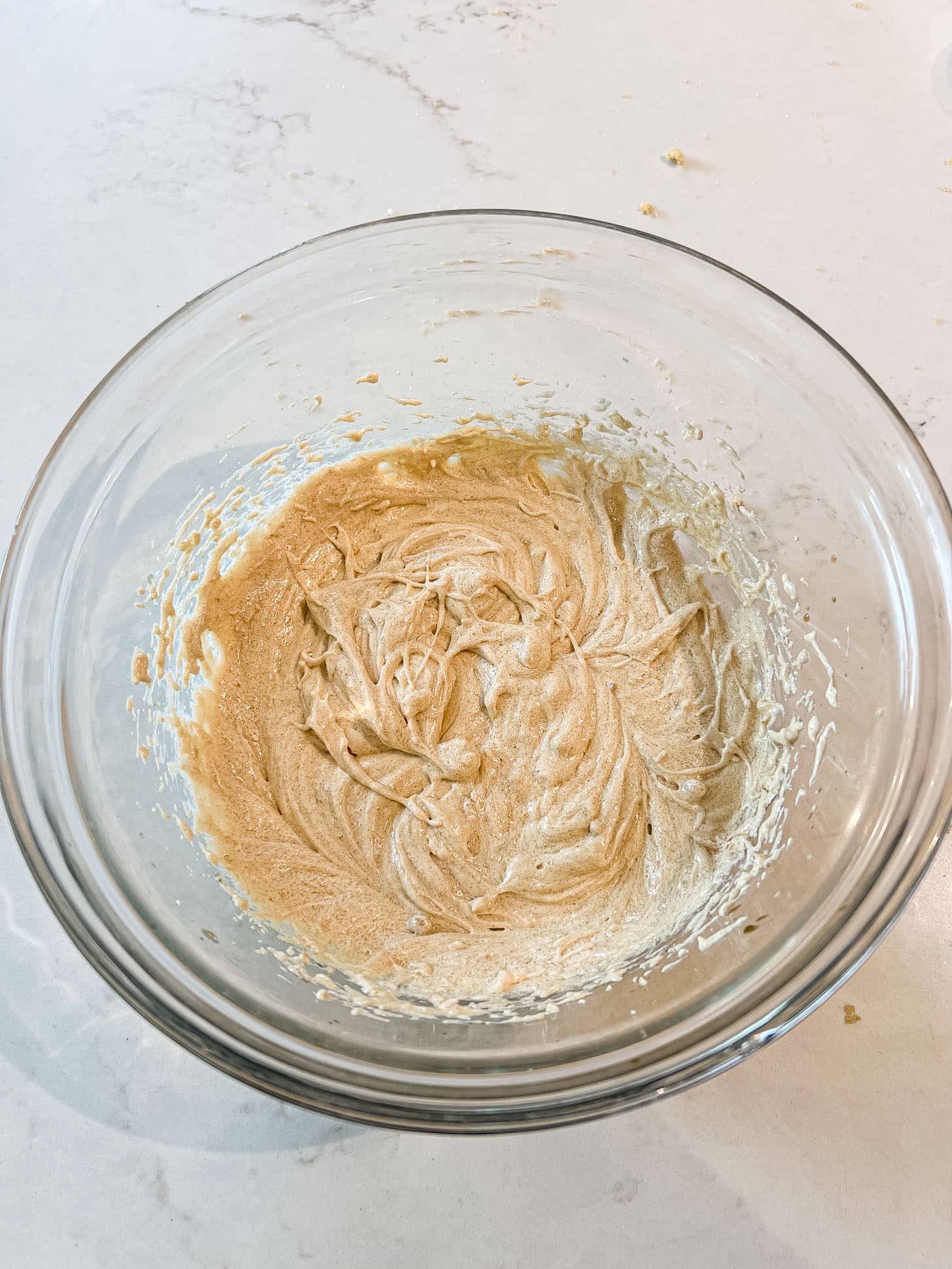 Butter and brown sugar creamed together in a glass mixing bowl until light and fluffy, on a white marble surface