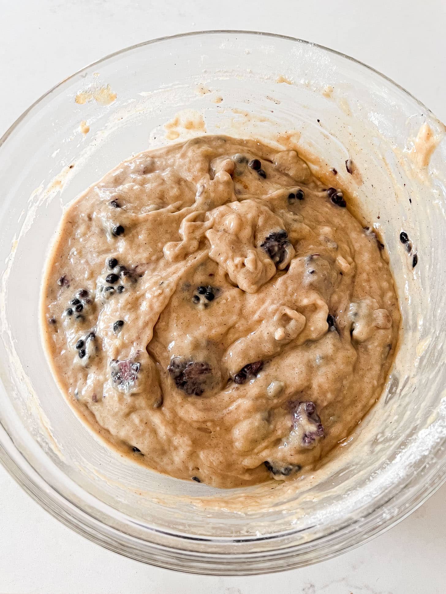 Completed blackberry banana bread batter with whole blackberries folded throughout in a glass mixing bowl, ready to pour into the loaf pan