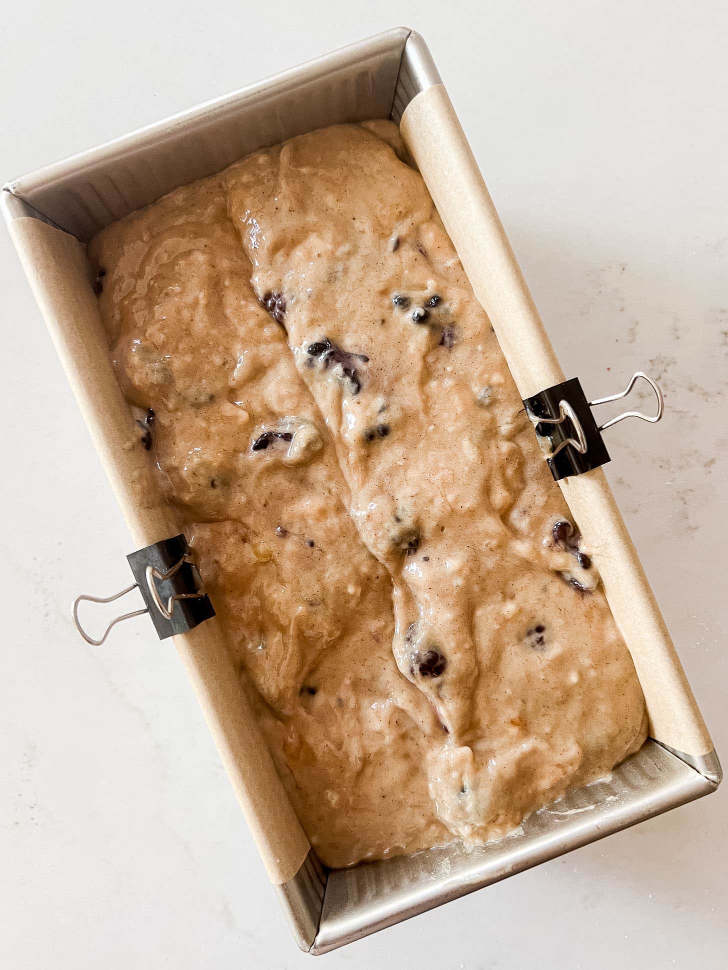 Blackberry banana bread batter with whole blackberries folded throughout, poured into a parchment-lined loaf pan secured with binder clips, ready to bake