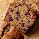 Close-up overhead view of sliced blackberry banana bread on parchment paper and a wooden board, showing the tender crumb loaded with blackberry pieces