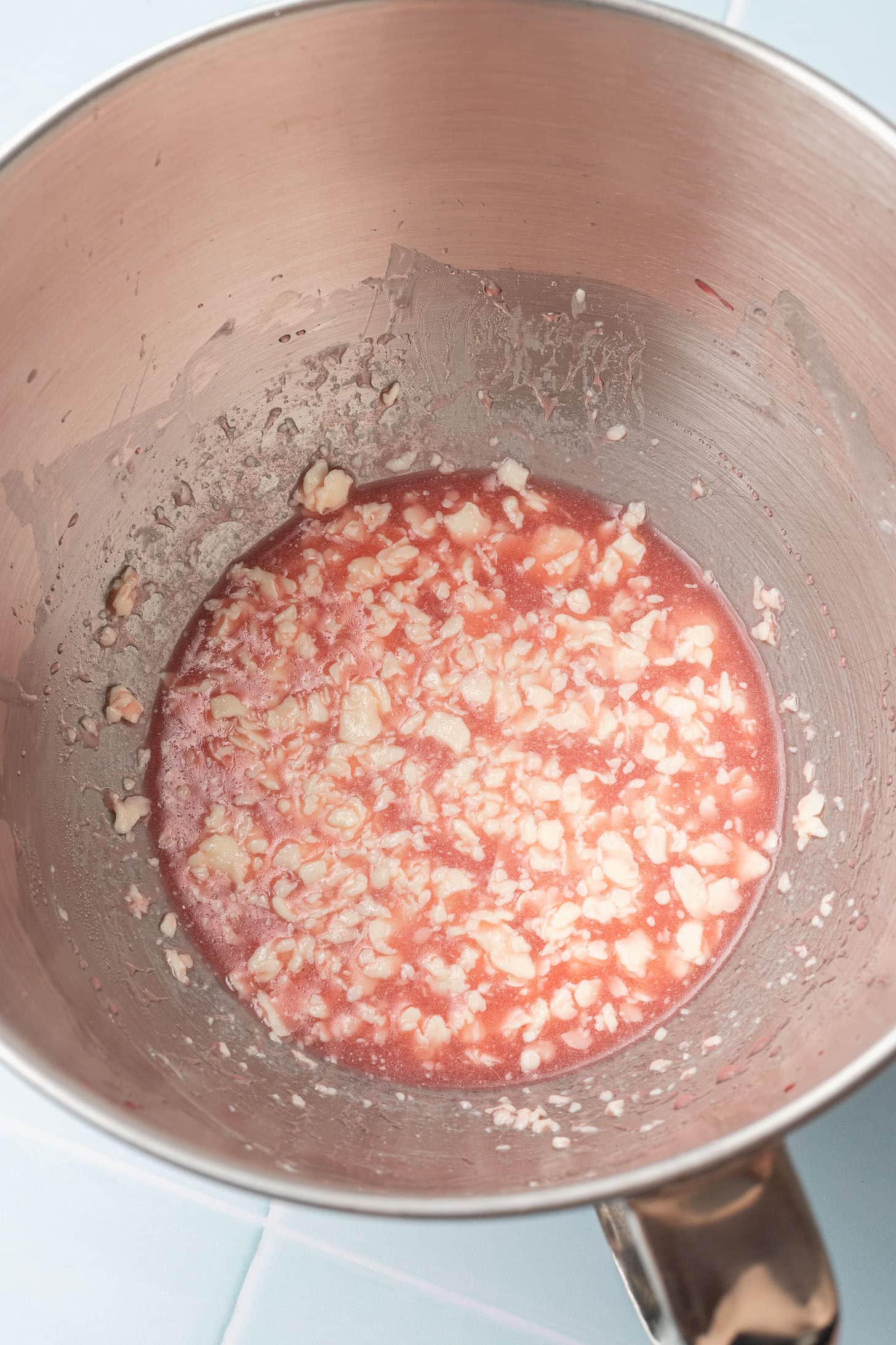 Overhead view of creamed butter, sugar, and maraschino cherry juice mixture in a stand mixer bowl, showing a pink and white marbled appearance