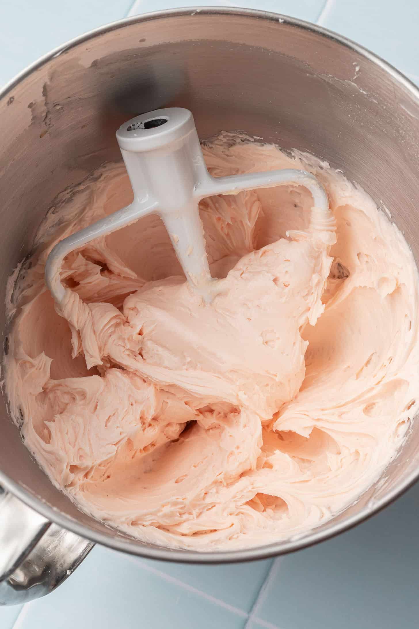 Fluffy cherry almond buttercream whipped to a soft blush pink color in a stand mixer bowl with the paddle attachment