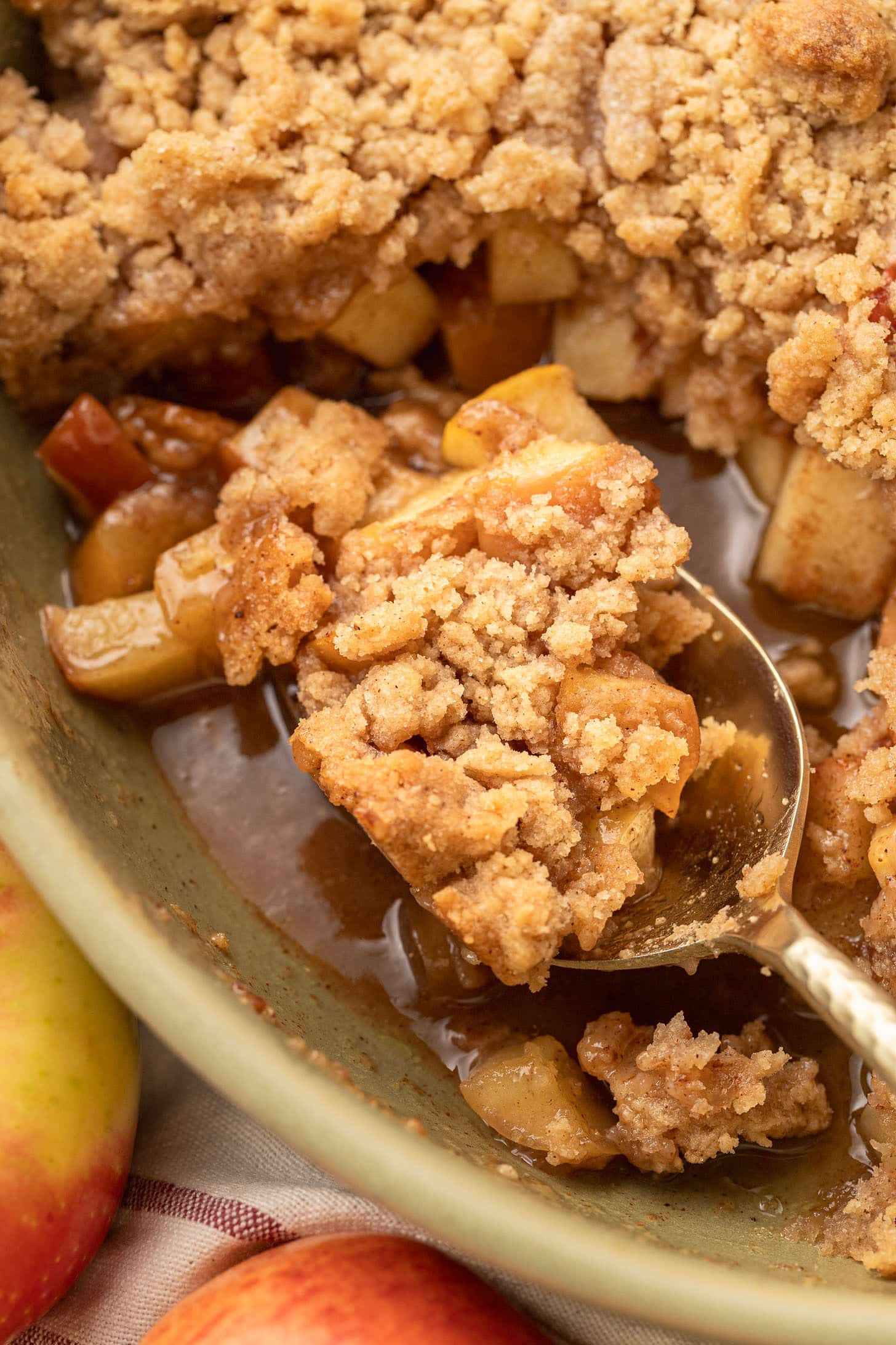 lose-up of a spoon scooping into a baked apple crumble, showing the gooey cinnamon apple filling beneath the golden crumble topping