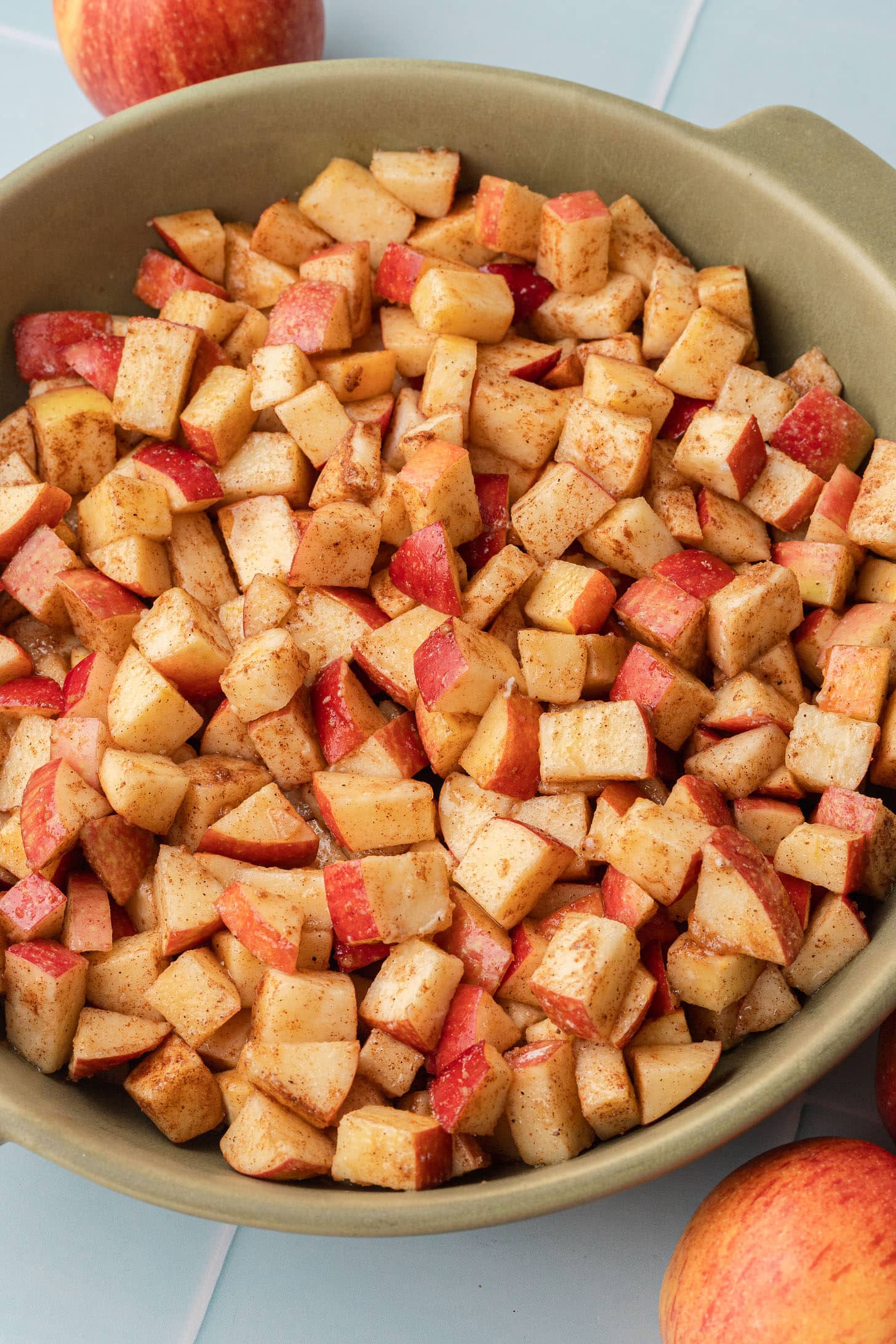Cinnamon-coated diced apples tossed together and spread in a green ceramic baking dish, ready to be topped with the crumble
